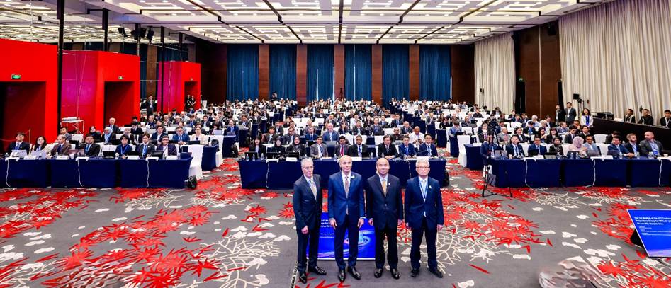 A group of men in suits standing in a room with chairs and tables

Description automatically generated